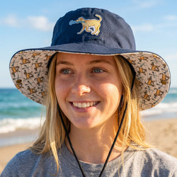 Person wearing a navy bucket hat with a dog design on a beach
