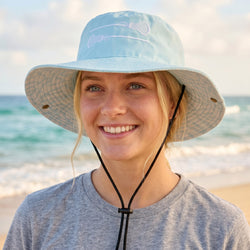 Woman wearing a light blue bucket hat with a lacrosse logo on a beach