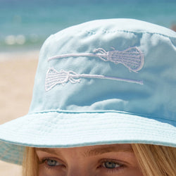 Light blue bucket hat with lacrosse stick design on a beach