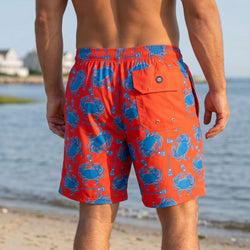 Person wearing red swim shorts with blue crab pattern by a body of water.