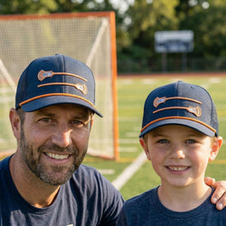 Man and young boy wearing matching blue lacrosse caps on a sports field