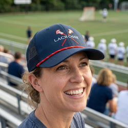 Person wearing a navy blue lacrosse cap with red accents on a sports field.