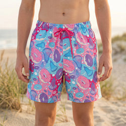 Person wearing colorful donut and lacrosse stick patterned swim trunks on a beach.