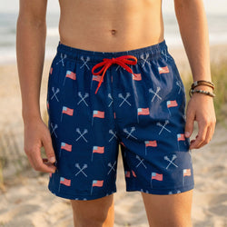 Person wearing blue lacrosse and usa flag paterned swim trunks on a beach.