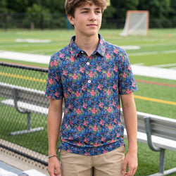 Prson wearing a tropical themed polo shirt with lacrosse pattern outdoors on a field.