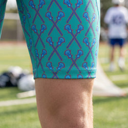 Green athletic shorts with blue lacrosse stick pattern worn by a person on a sports field.