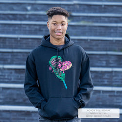 Person wearing a black hoodie with a colorful lacrosse stick head and donut design, standing against a brick wall.