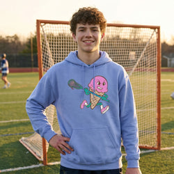 Person wearing a blue hoodie with a pink ice cream cone and lacrosse stick design on a soccer field.