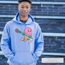 Person wearing a blue hoodie with a colorful lacrosse graphic design in front of a brick wall.