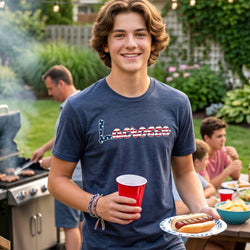 Young man wearing a lacrosse tee holding a red cup and a plate with a hot dog at a barbecue party in a backyard.