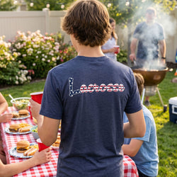 Person wearing a blue t-shirt with 'Lacrosse' printed on it at a backyard barbecue.