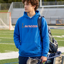 Person wearing a blue hoodie with lacrosse text, holding a lacrosse stick on a sports field.