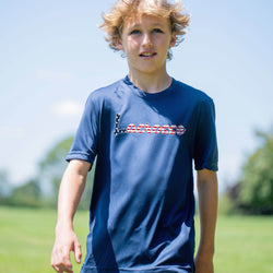 Young boy wearing a blue t-shirt with 'Lacrosse' printed on it, standing outdoors.
