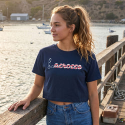 Woman wearing a navy blue t-shirt with 'Lacrosse' printed on it, standing by a waterfront.