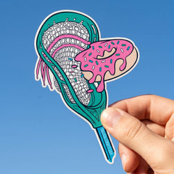 Hand holding a colorful sticker of a lacrosse stick with pink and white design against a blue background