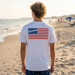 Person wearing a white t-shirt with a lacrosse-themed design on the beach