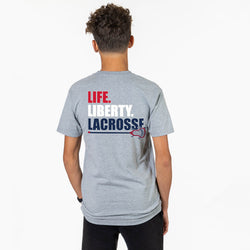 Person wearing a gray tee with Life Liberty Lacrosse text with lacrosse stick design.