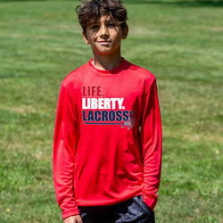 Child wearing a red long-sleeve shirt with 'Life. Liberty. Lacrosse' text on a grassy background