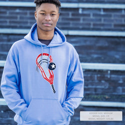 Person wearing a blue hoodie with a lacrosse design against a brick wall.