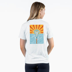 Woman wearing a white t-shirt with sunset lacrosse design on the back, standing against a white background.