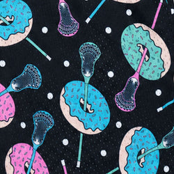 A close-up of a patterned fabric featuring lacrosse sticks and donuts in bright blue, pink, and teal on a black background with white lacrosse balls.