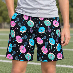 Teen wearing shorts with lacrosse and donut pattern outdoors on a lacrosse field.