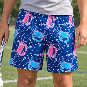 Teen wearing blue shorts with lacrosse stick and crab pattern holding a pacrosse stick outdoors on a field.