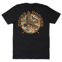 A black short-sleeve t-shirt shown flat against a white background, featuring a large back graphic with the words 'DUCKS & DODGES' in tan around a circular camouflage design with a duck and crossed sticks.