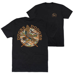 Two black short-sleeve t-shirts shown on a white background, with the back view in front and the front view behind. The back shirt features a large circular graphic with a duck, crossed paddles, and the words “Ducks & Dodges” in tan over a camouflage circle.