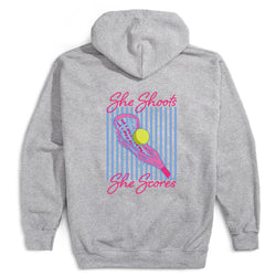 A heather gray hoodie shown from the back, featuring a colorful graphic print of a lacrosse stick, a yellow ball, and pink text reading 'She Shoots She Scores' over a blue striped background.