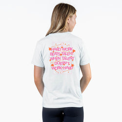 A woman shown from the back wearing a white t-shirt with a pink graphic text design that reads 'HARD WORK BEATS TALENT WHEN TALENT DOESN'T WORK HARD!' with small orange stars.