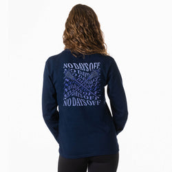 A woman viewed from behind wearing a navy blue long-sleeve shirt with a large light blue graphic print on the back. The graphic features the text 'NO DAYS OFF' repeated in a pattern with crossed sticks.