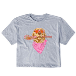 A light heather gray short-sleeve t-shirt featuring a graphic print of a golden retriever dog wearing orange sunglasses and a pink bandana, holding a pink lacrosse stick.