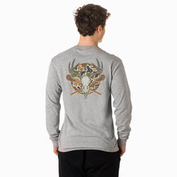 A man viewed from behind wearing a heather gray long-sleeve shirt with a large back graphic featuring a deer skull, antlers, crossed lacrosse sticks, and a camouflage pattern, paired with black pants against a white studio background.
