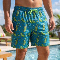 Person wearing green swim shorts with green pickle pattern by a pool.