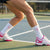 Person wearing white socks with pink pickleball accents and tennis shoes on a tennis court.