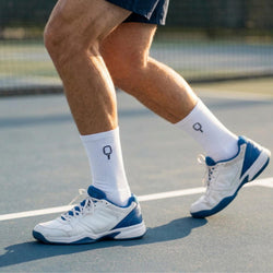 Person wearing white and blue athletic shoes and pickleball socks on a tennis court