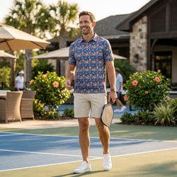 Man in a floral picklball polo shirt and shorts holding a paddle on a tennis court.