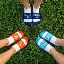 Three pairs of feet wearing socks with motivational text on a grassy background