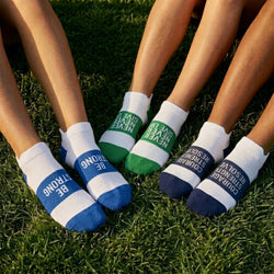 Three sets of feet with motivational socks on them sitting in grass
