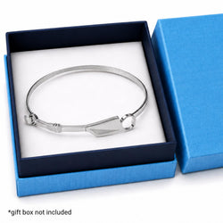 A polished silver-toned metal bangle bracelet with a geometric triangular charm, presented inside an open dark blue gift box with a white insert. A blue box lid is visible on the right, and a text overlay at the bottom left reads '*gift box not included'.