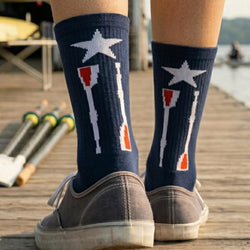 Person wearing navy socks with a star and oars design on a wooden dock.