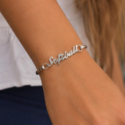 A close-up of a person's wrist wearing a silver script bracelet that reads 'Softball' with a small clear accent.