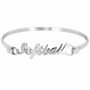 A silver metal bangle bracelet featuring the word 'Softball' in cursive script, with a small clear accent between the letters, shown on a plain white background.