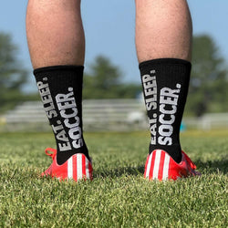 Black mid-calf soccer socks featuring large white Eat Sleep Soccer text on the back.