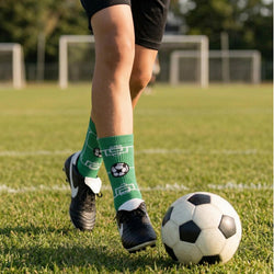 Person on a soccer field wearing green socks with a soccer ball design, standing next to a soccer ball.