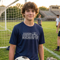 Young man wearing a 'Just Kickin' It' t-shirt on a soccer field