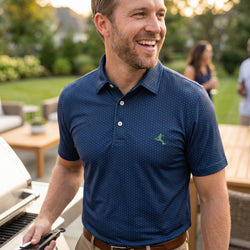 Man wearing a blue polo shirt with a soccer logo, standing outdoors in a garden setting.