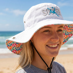 Person wearing a white bucket hat with colorful soccer brim on a beach