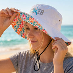 Person wearing a white bucket hat with colorful soccer brim on a beach